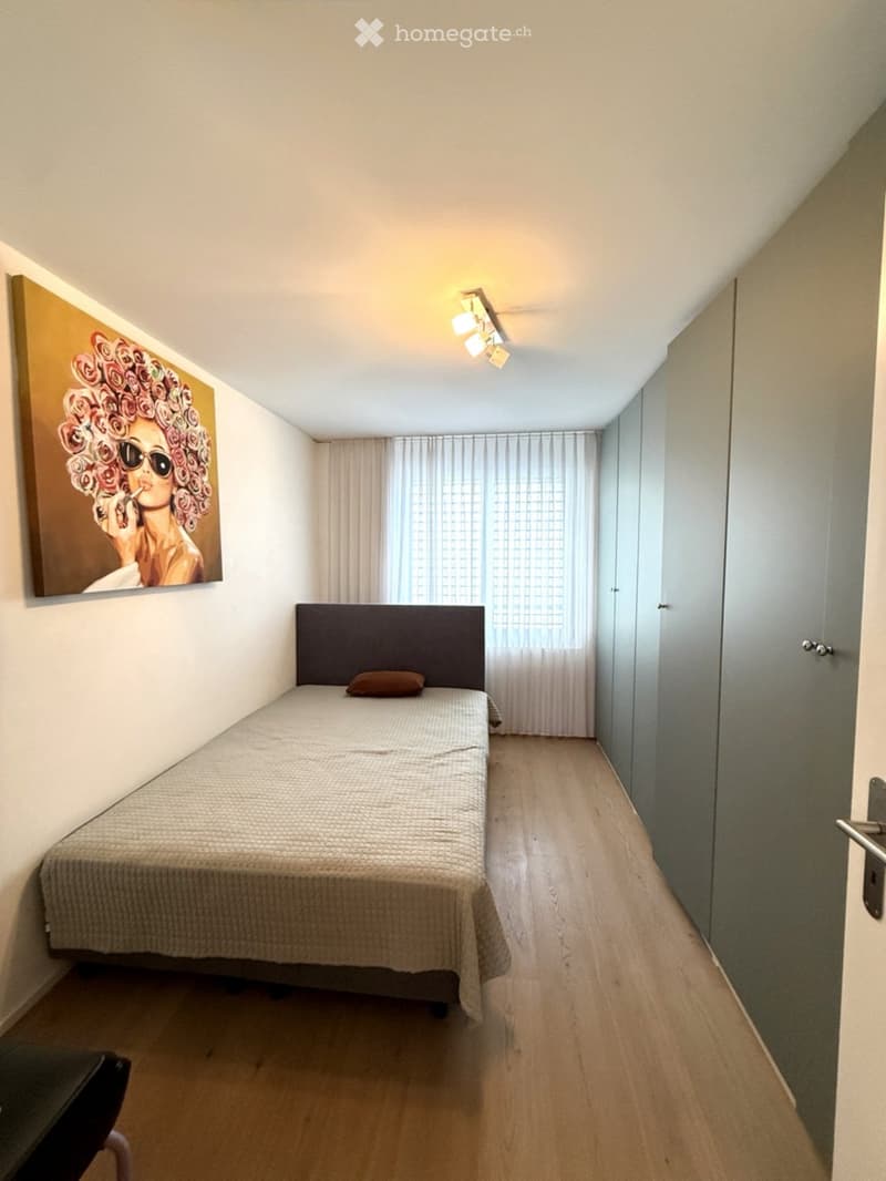 Minimalist bedroom with a single bed, a small pillow, a large painting on the wall, and light-colored curtains covering a window.