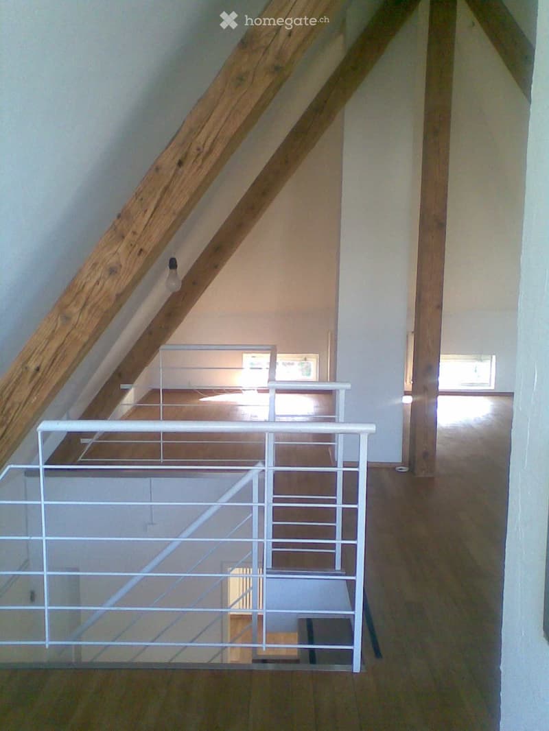 Wooden staircase with white metal railing, wooden walls, and a view of a room below with a desk and framed pictures on the wall.