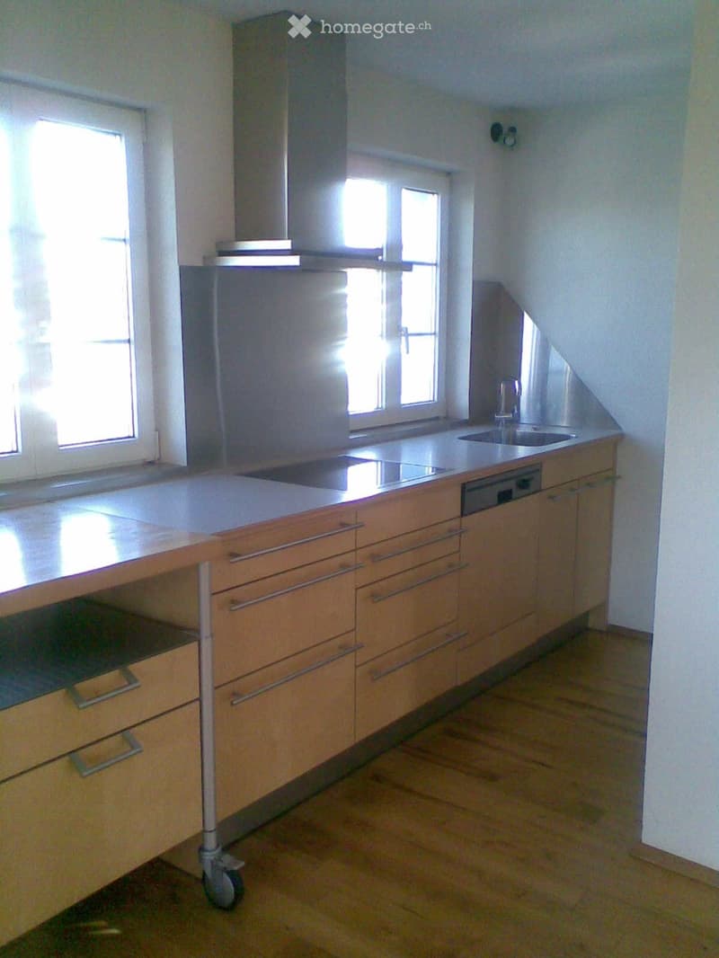 Modern kitchen with light wooden cabinets, stainless steel appliances, and a central island with a sink and range hood.