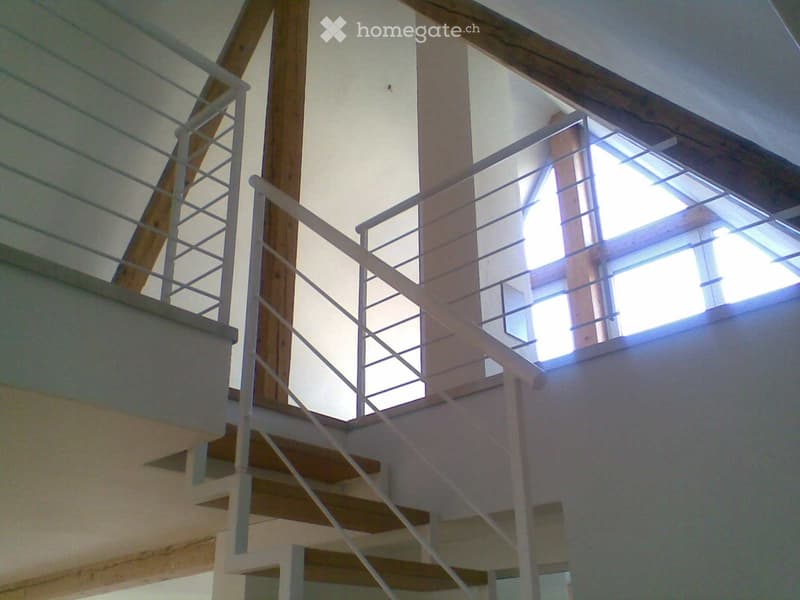 Modern interior staircase with wooden steps, white metal railing, and large skylight windows allowing natural light to fill the space.