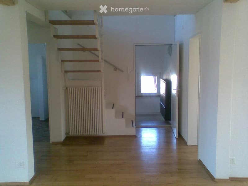 Empty hallway with wooden flooring, white walls, a staircase leading upwards, and a radiator on the left side.