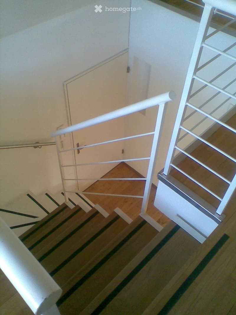 Wooden staircase with white railing and striped carpet runner, leading to a closed door.