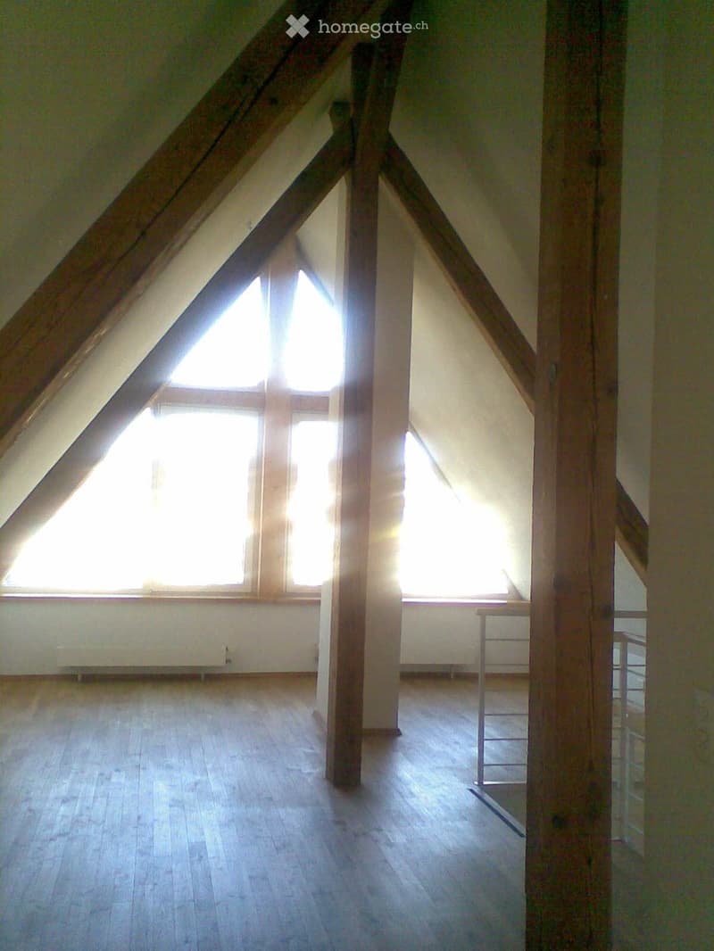 Empty attic space with wooden beams, wooden flooring, and large windows allowing natural light to enter.