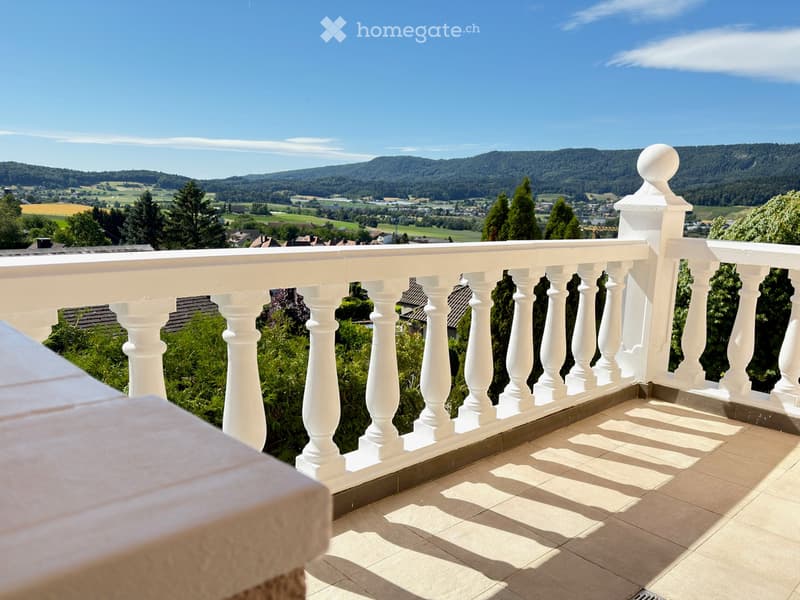 Balcony with white balustrade overlooking a scenic valley and hills.