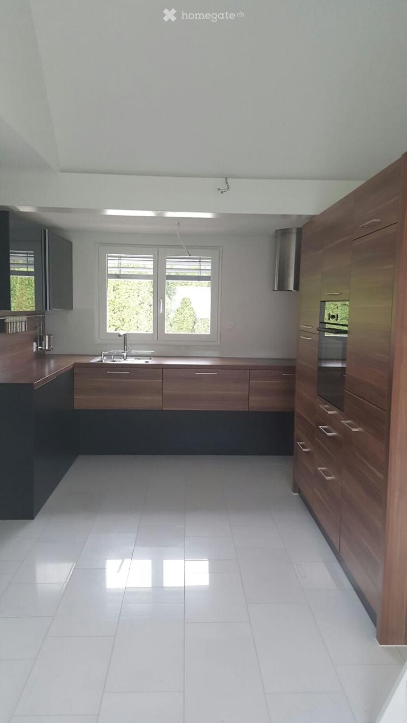 Modern kitchen with white tiled floor, wooden cabinets, stainless steel sink, and built-in oven. Large window provides natural light.