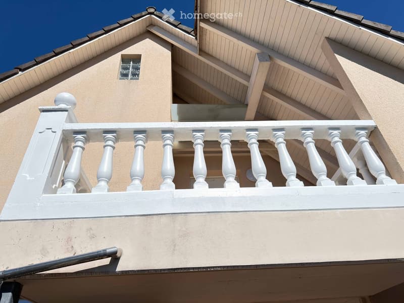 Balcony with white balustrade and beige walls, featuring a small window above.