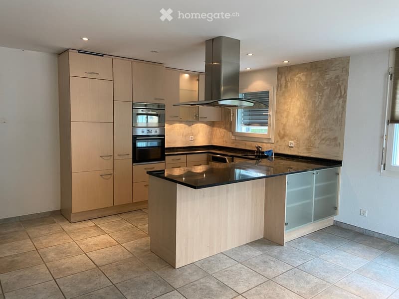 Modern kitchen with light wood cabinets, stainless steel oven, island with black countertop, and built-in sink.