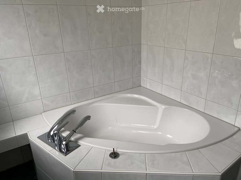 Modern bathtub with sleek chrome faucet and matching trim, set in a tiled corner with grey marble tiles.