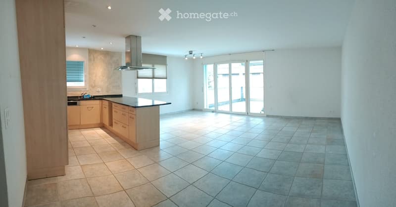 Modern kitchen with light wooden cabinets, a central island, and a large window overlooking a balcony. The space features tiled flooring and recessed lighting.