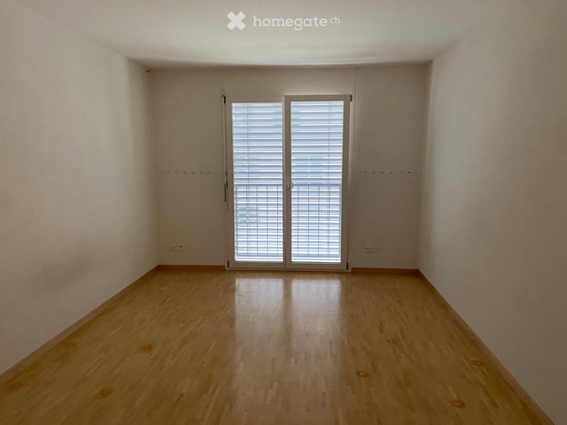 Empty room with light wooden flooring, white walls, and a large window with blinds.