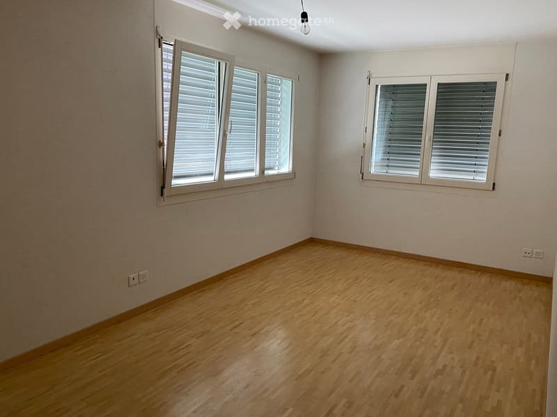 Empty room with wooden flooring, white walls, and multiple windows with blinds.