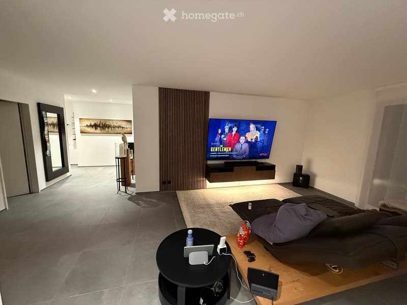 Modern living room with a sofa, coffee table, TV, and artwork on the wall. The space features a large window and a sleek design.
