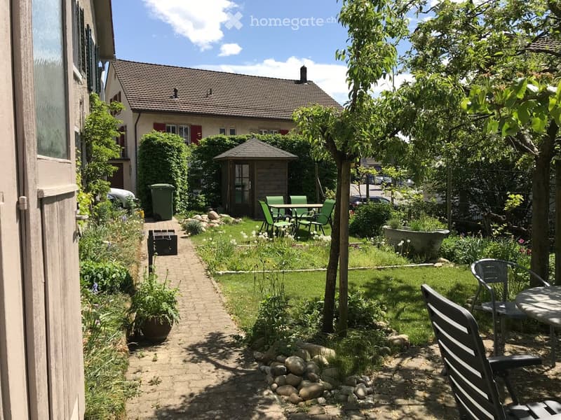 Well-maintained garden with a brick pathway, seating area, small gazebo, and surrounding greenery.