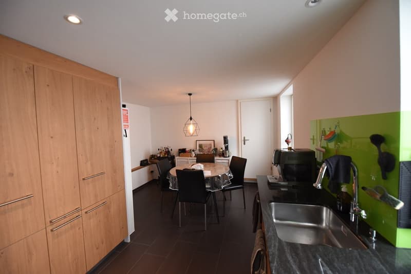 Modern kitchen with dark tiled floor, wooden cabinets, stainless steel sink, coffee machine, and a small dining area with a round table and chairs.