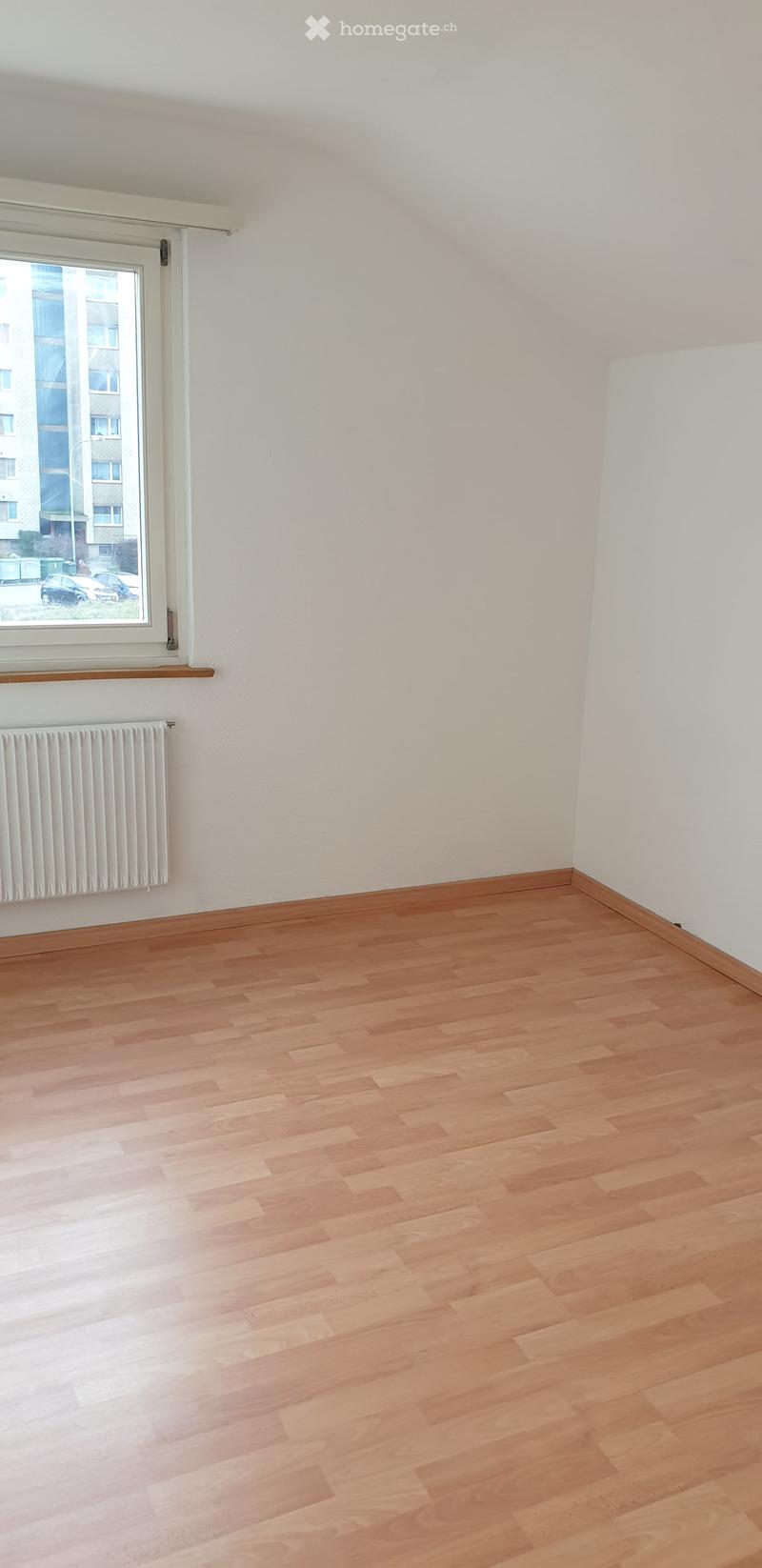 Empty room with wooden flooring, white walls, a window with a radiator below, and a small shelf above the radiator.