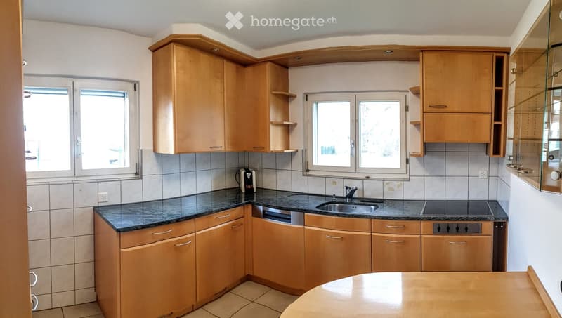 Modern kitchen with light wooden cabinets, granite countertop, stainless steel sink, dishwasher, and coffee maker.