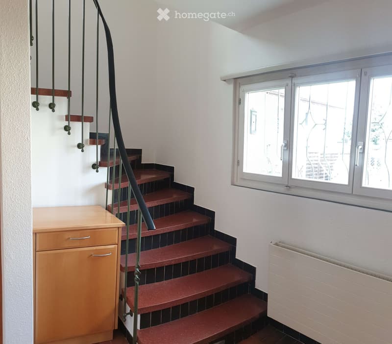 Staircase with red carpeted steps and a black metal railing, adjacent to a wooden cabinet and a window with white frame and blinds.