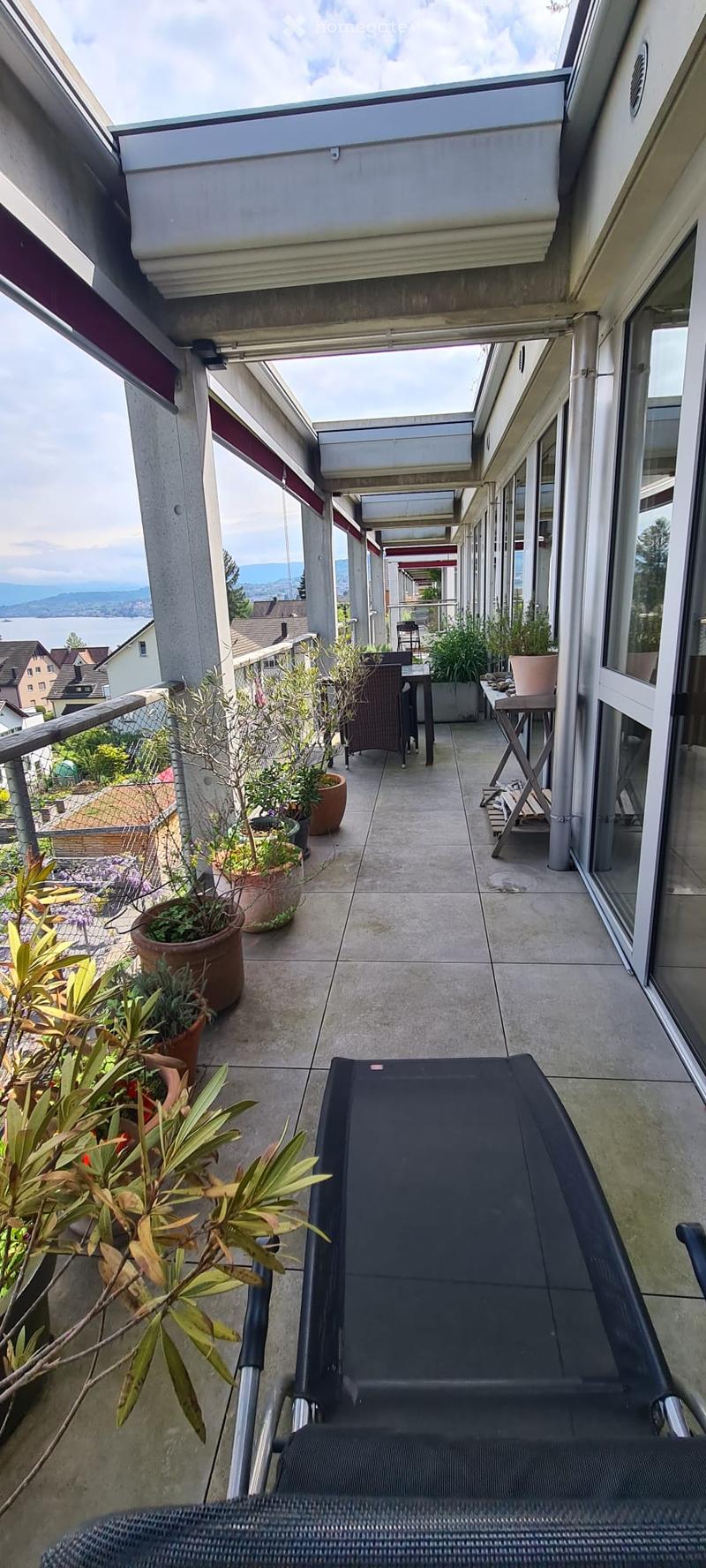 Balcony with a view of the lake and surrounding landscape, featuring potted plants, a chair, and a small table.