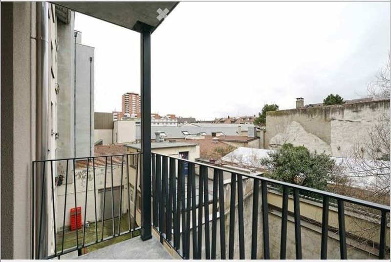 Balcony with metal railing overlooking a cityscape with buildings and rooftops.