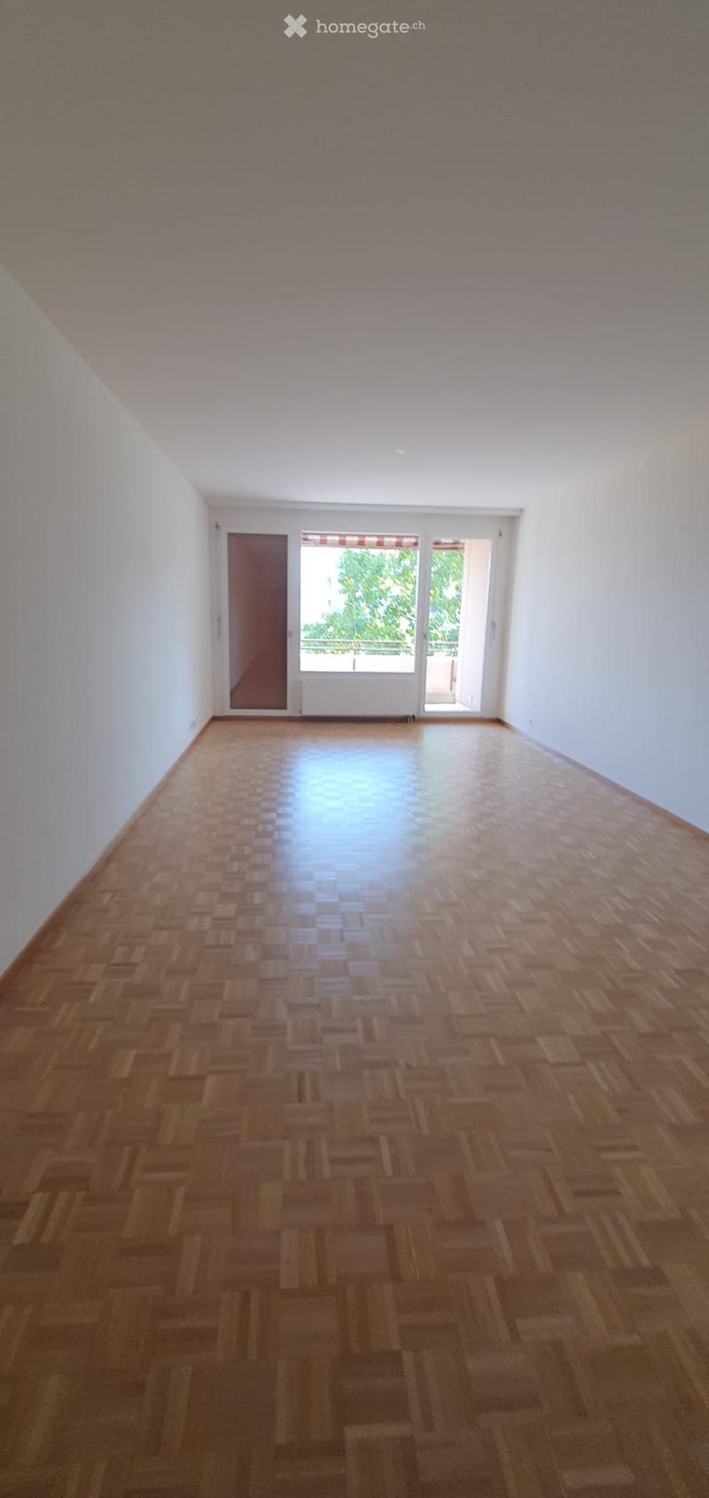 Empty room with wooden parquet flooring, white walls, and large windows with blinds. No furniture or equipment present.