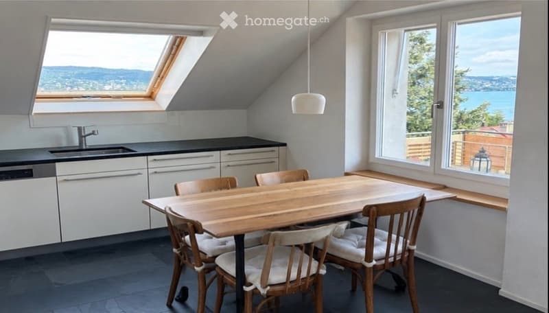 Modern kitchen with white cabinets, black countertops, a wooden dining table, and chairs, large windows offering a scenic view.
