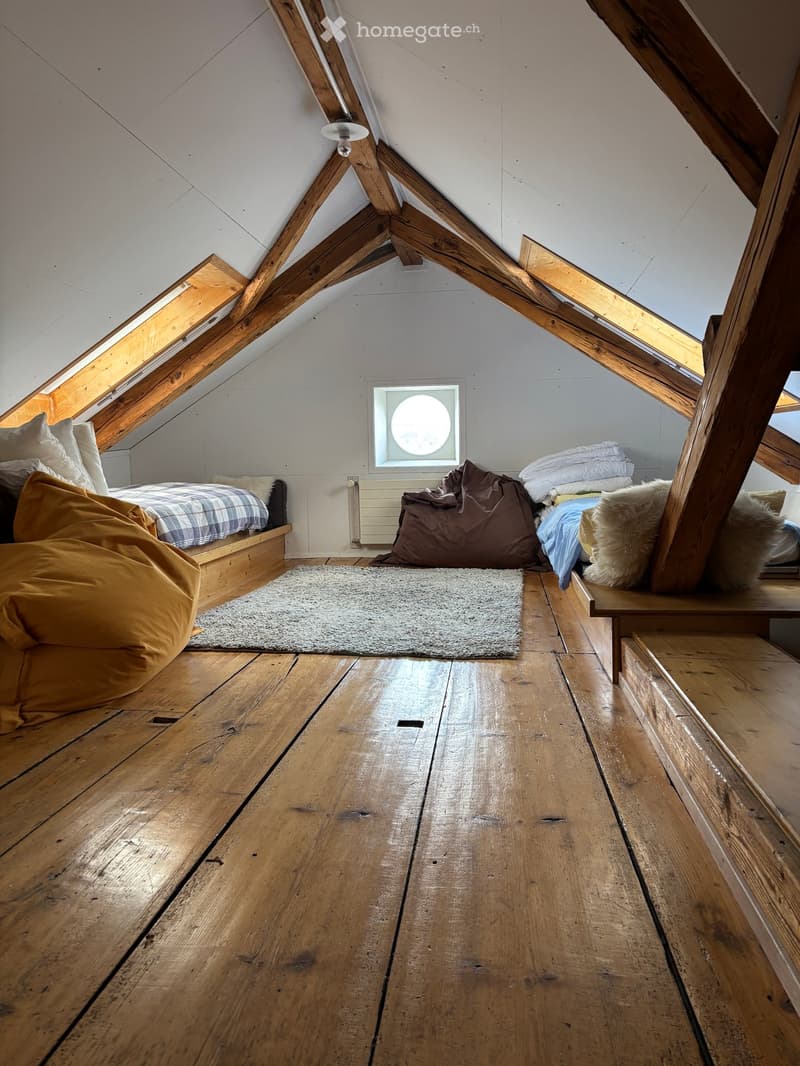 Cozy attic bedroom with wooden beams, skylights, a bed, bean bag chairs, and a small bench.