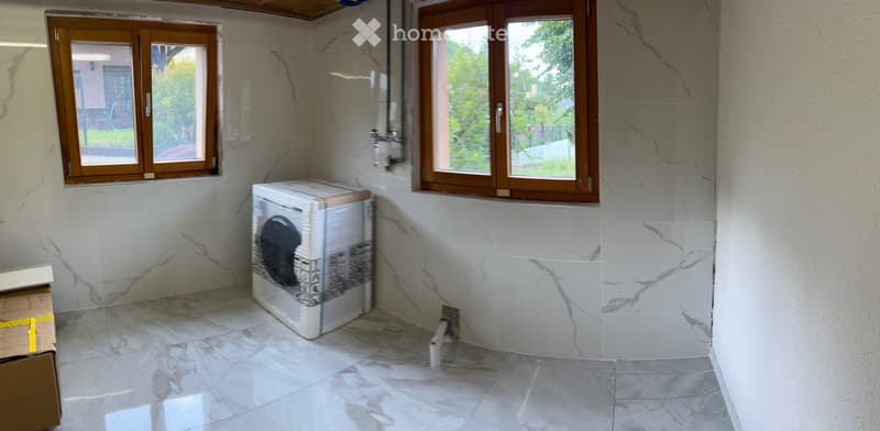 Empty room with marble walls and floor, two windows, and a washing machine in the corner.