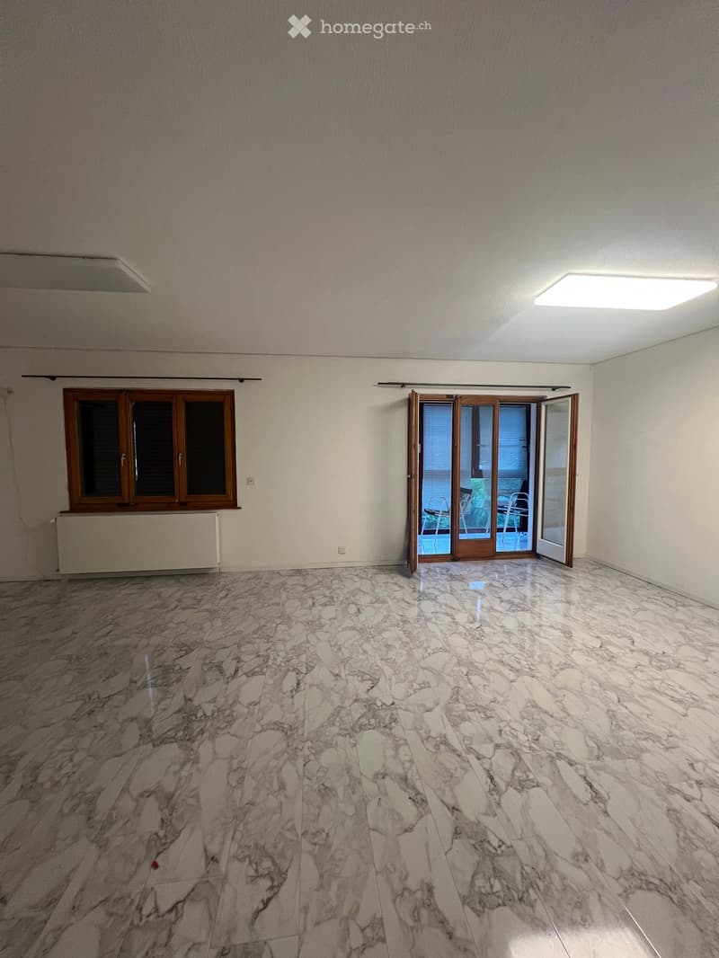 Empty room with marble flooring, large window with wooden frame, sliding glass door leading to balcony, and white walls.