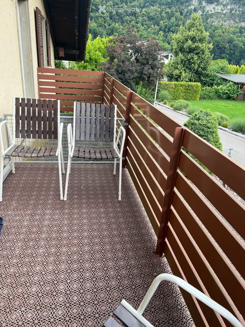 Balcony with wooden railing, patterned floor, and several chairs and a table.