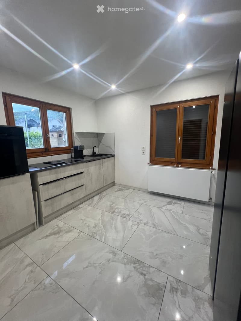 Modern kitchen with marble flooring, white cabinets, and stainless steel appliances. Features a sink, faucet, coffee maker, and radiator.
