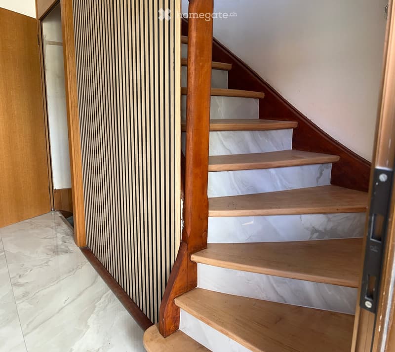 Wooden staircase with white marble risers, wooden handrail, and open wooden door frame leading to another area.