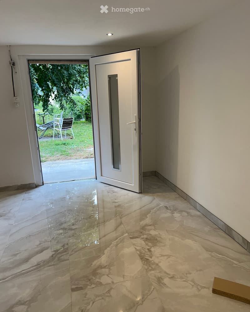 Empty hallway with polished marble flooring, white walls, and a sliding glass door leading to an outdoor area.