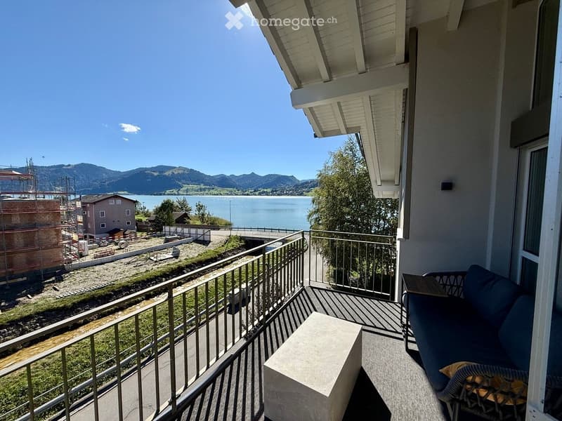 Balcony with a view of a lake and mountains, featuring a sofa and a small table.