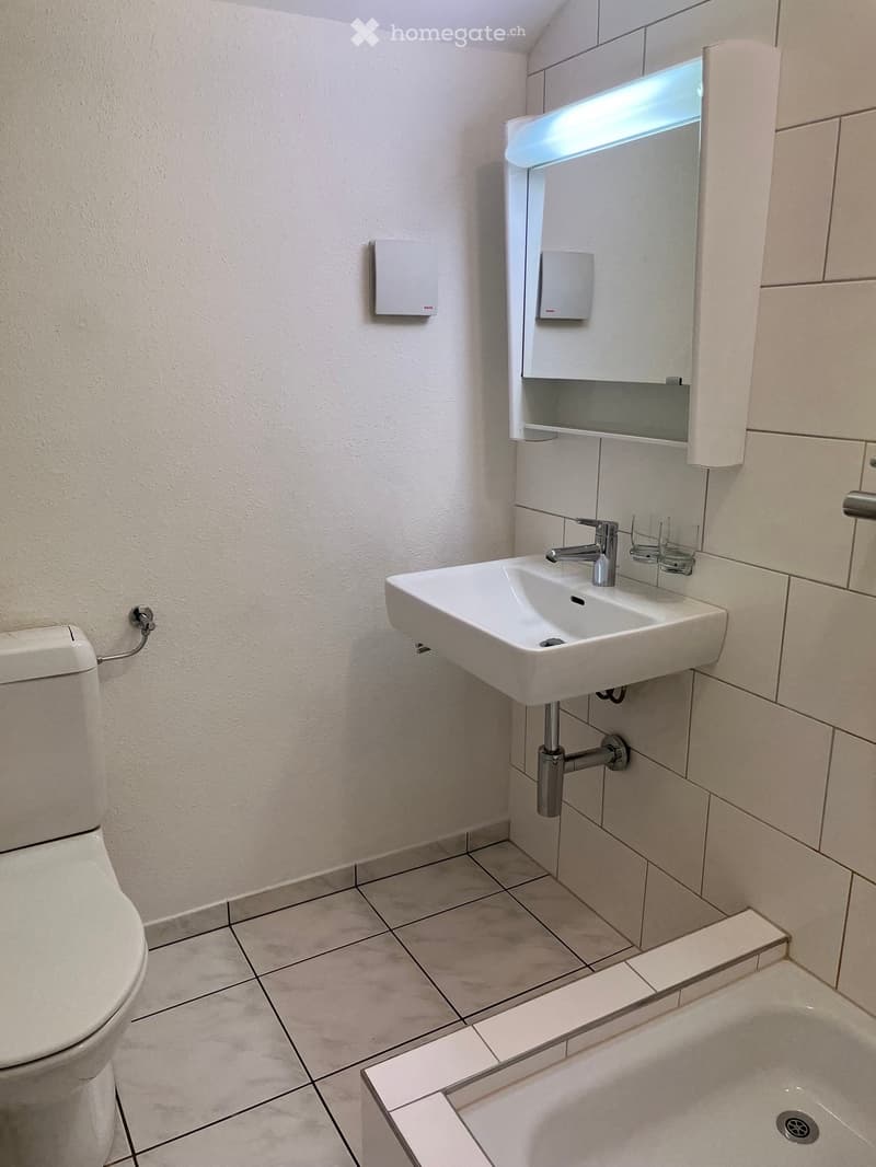 Modern bathroom with white tiled walls, a toilet, a sink with a modern faucet, a mirror with built-in lighting, and a bathtub.