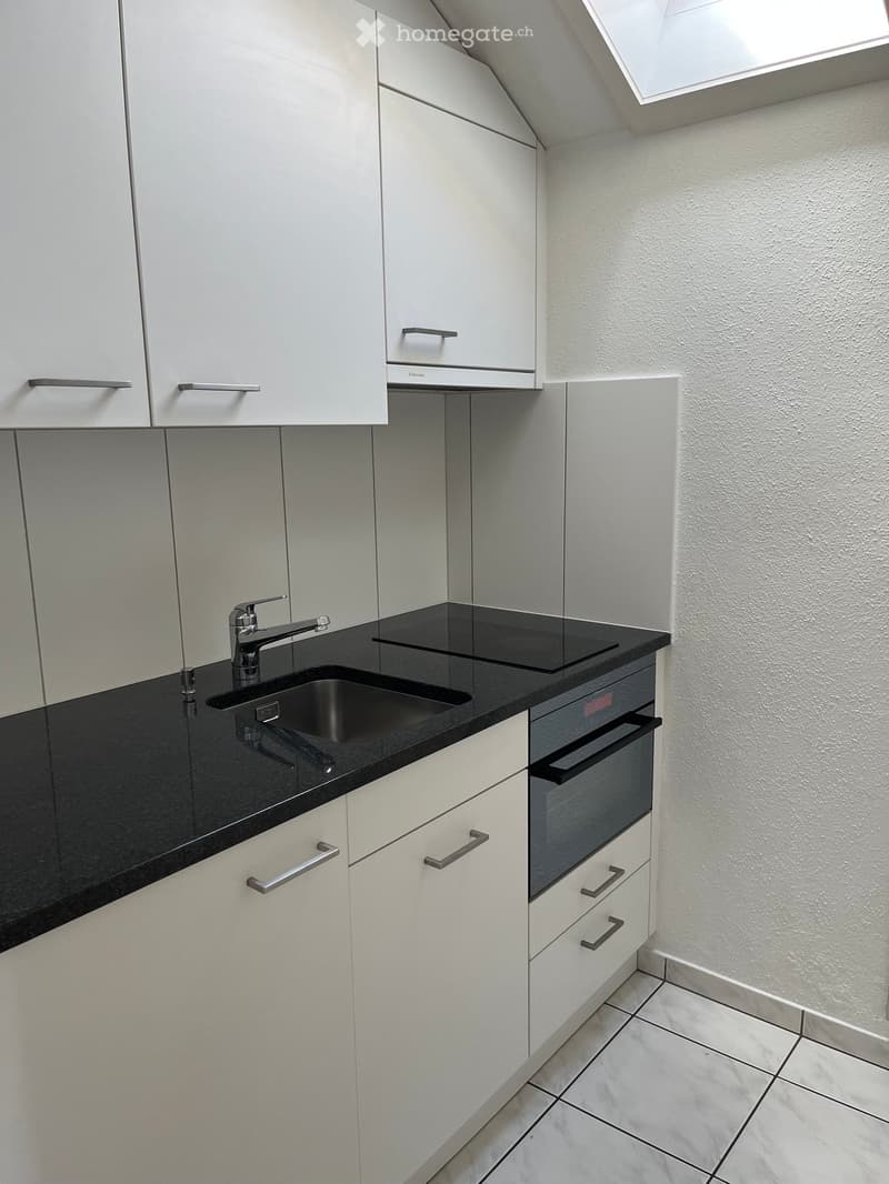 Modern kitchen with white cabinets, black countertop, stainless steel sink and faucet, built-in oven, and sleek design.