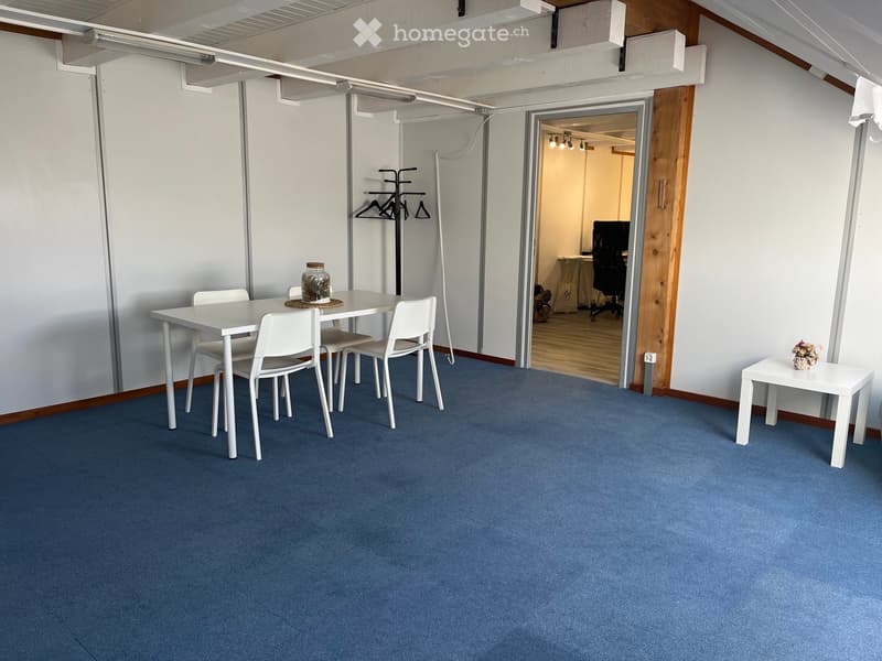 A furnished room with a white dining table and chairs, a small side table with a flower vase, a coat rack, and an open doorway leading to another room with a desk and chair.