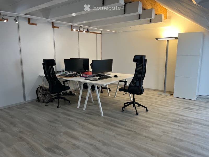 Modern office space with a white desk, two ergonomic chairs, multiple monitors, and a backpack on the floor.