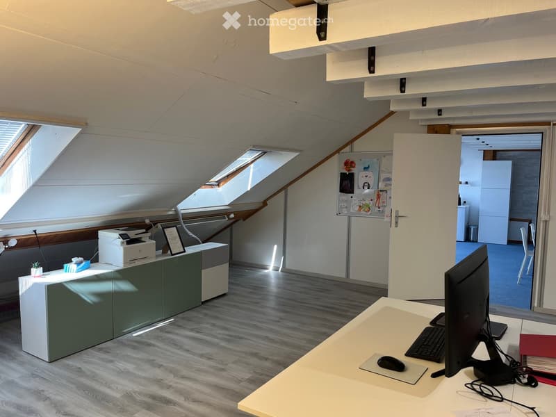 Office space with wooden flooring, large windows, desks, chairs, computer equipment, printer, and a small refrigerator.
