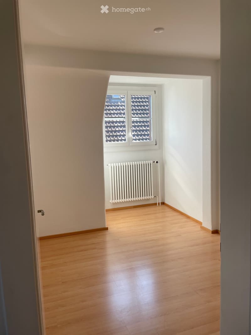 Empty room with wooden flooring, white walls, and a radiator under a window with decorative glass panels.