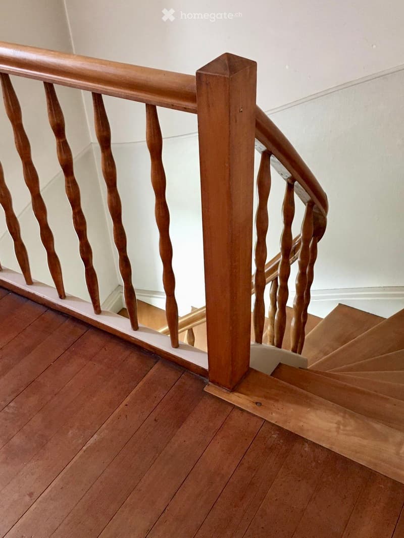 Wooden staircase with a polished wooden handrail and balusters, featuring a classic design with turned balusters and a square newel post.