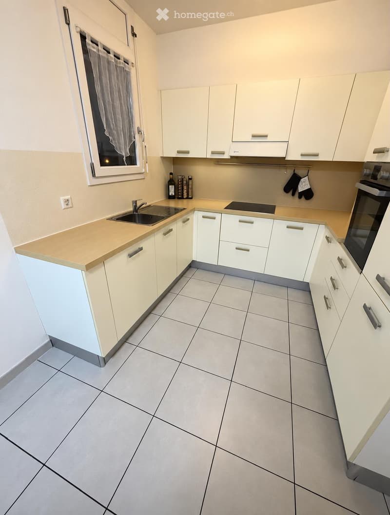Modern kitchen with white cabinets, tiled floor, sink, oven, and countertop.