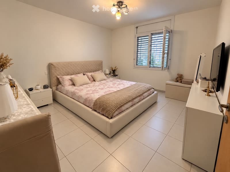 A well-lit bedroom with a large bed, nightstands, a chair, a mirror, and decorative items.
