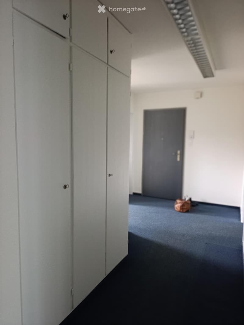 Empty hallway with grey cabinets on one side, a closed door at the end, and a small brown bag on the floor.