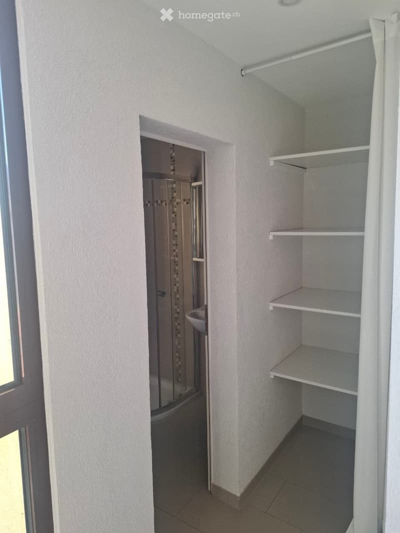 Empty room with built-in shelves and a doorway leading to a small bathroom.