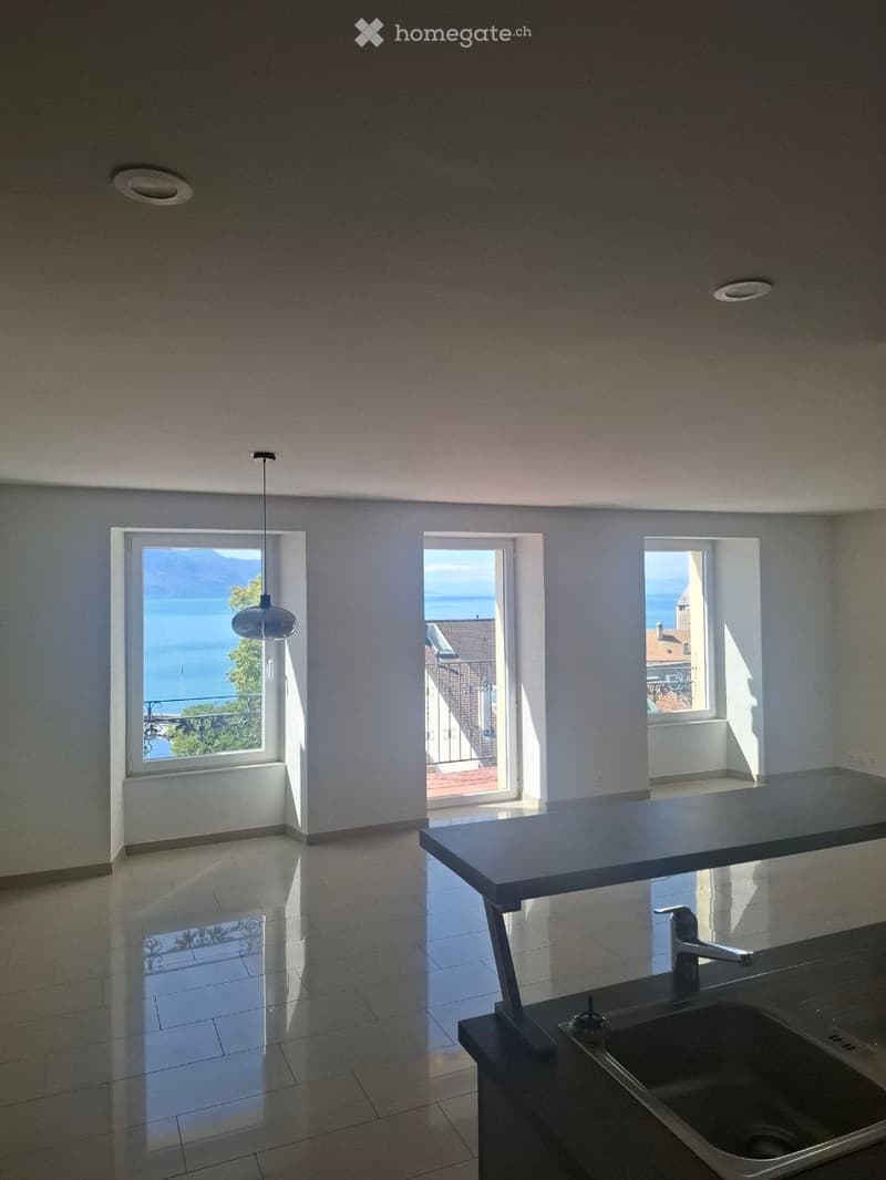 Empty kitchen with modern design, large windows overlooking a scenic lake view, and a sleek countertop with a sink.
