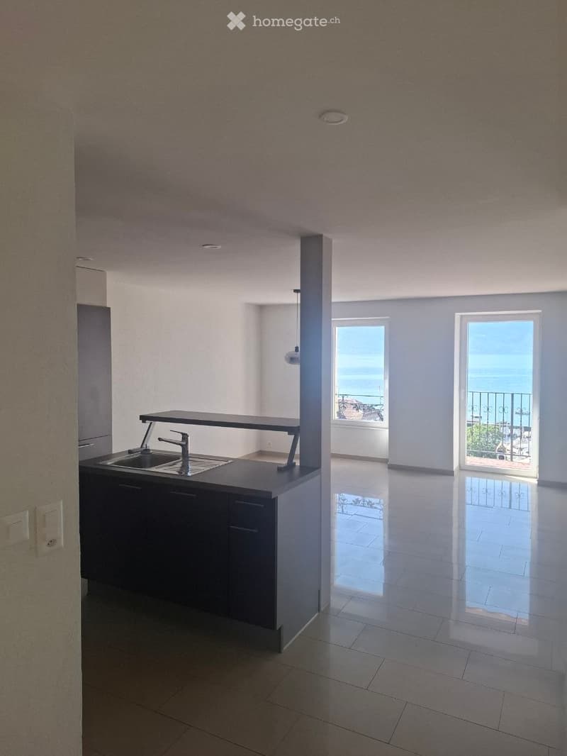 Empty kitchen area with a sink, countertop, and a view of a balcony overlooking the sea.