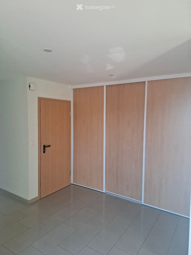 Empty room with tiled floor, white walls, and a wooden door. No furniture or equipment is present.