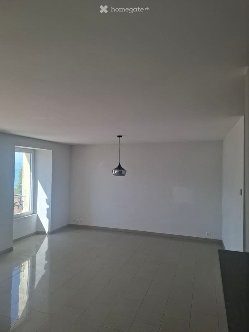 Empty room with tiled floor, white walls, and a single pendant light fixture. Natural light enters through a window on the left side.