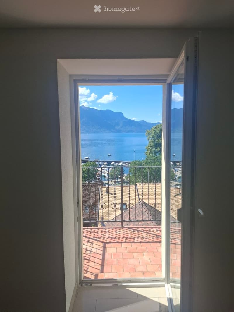 Open balcony with a view of a lake and mountains, featuring a metal railing and tiled floor.