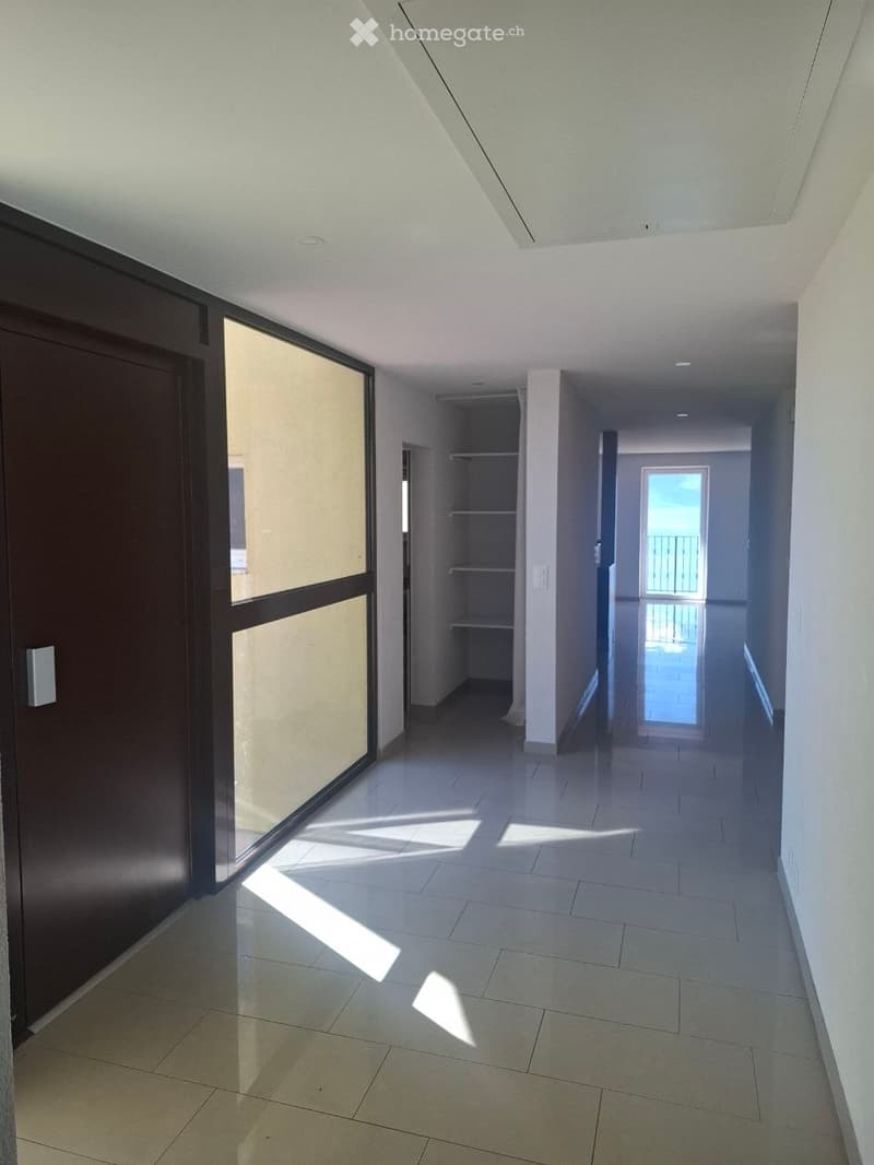 Empty hallway with tiled floor, white walls, and large glass doors leading to a balcony area.